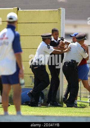 NUR FÜR REDAKTIONELLE VERWENDUNG - KEIN KOMMERZIELLER VERKAUF: England Cricketer Marcus Trescodick (links) beobachtet, wie ein Eindringling von der lokalen Polizei aus der Team-Netzsitzung in Kapstadt entfernt wird. * die Mannschaft plant, am Freitag nach East London zu reisen, nachdem sie beschlossen hat, ihr geplantes Spiel morgen in Simbabwe nicht zu spielen. Stockfoto