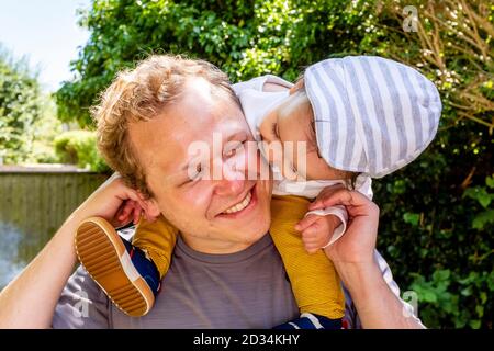 Ein kleines Kind, das seinen Onkel küssend, während es auf seinen Schultern sitzt, East Sussex, Großbritannien. Stockfoto