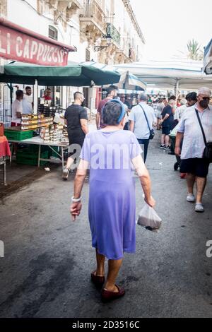 Ältere Frau, die in einem lila Kleid auf dem Markt von Ortigia. Ortygia Markt in Syrakus. Ortygia ist eine Insel in der sizilianischen Stadt Syrakus, ON Stockfoto