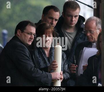 MIT ZUSÄTZLICHEN BILDUNTERSCHRIFTEN ÜBERLIEFERT MELANIE Jones die Mutter des ermordeten Schuljungen Rhys Jones hält eine Kerze mit Pater Andrew Unsworth, während Ehemann Stephen und Sohn Owen auf eine Gemeinschaft Vigil im Croxteth Park, Liverpool, schaut. Stockfoto