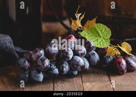 Nahaufnahme von Trauben lila mit Weinflasche in Hintergrund auf einer rustikalen Holzoberfläche Stockfoto