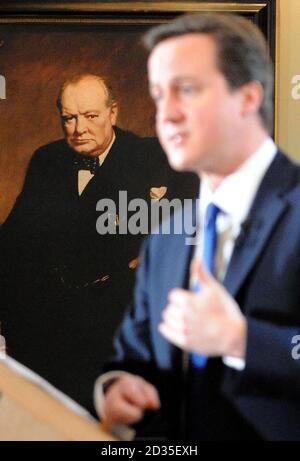 Der Vorsitzende der Konservativen Partei David Cameron wird von einem Porträt des Ministerpräsidenten Winston Churchill aus dem Krieg übersehen und spricht auf seiner regelmäßigen Pressekonferenz im St. Stephen's Club in Westminster. Stockfoto
