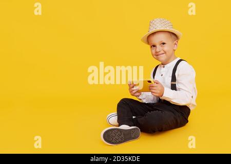 Niedliche smilling Kind Junge mit Smartphone auf gelbem Hintergrund. Werbung für pädagogische Anwendungen auf einem Handy für Kinder. Lustiges Gesicht. Stockfoto