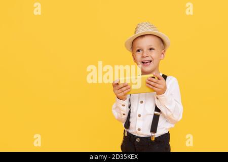 Niedliche smilling Kind Junge mit Smartphone auf gelbem Hintergrund. Werbung für pädagogische Anwendungen auf einem Handy für Kinder. Lustiges Gesicht. Stockfoto