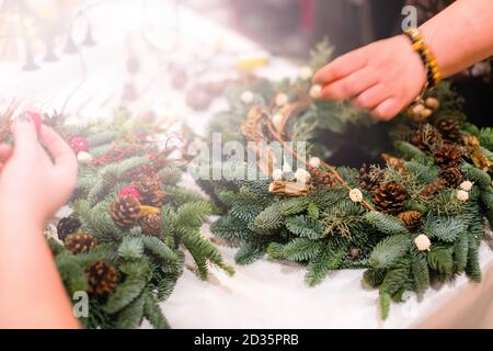 Weihnachten Kranz Weberei. Frau Hände verzieren holiday Wreath der Fichte Äste, Kegel und verschiedenen organischen Dekorationen auf dem Tisch Stockfoto