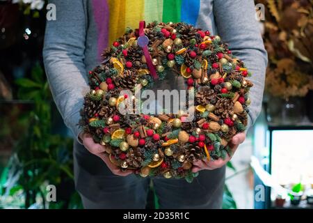 Person hält schöne und bunte Hand gemacht Weihnachtskranz, grüne Fichtenzweige mit Tannenzapfen und andere Dekorationen dekoriert. Weihnachtslch Stockfoto