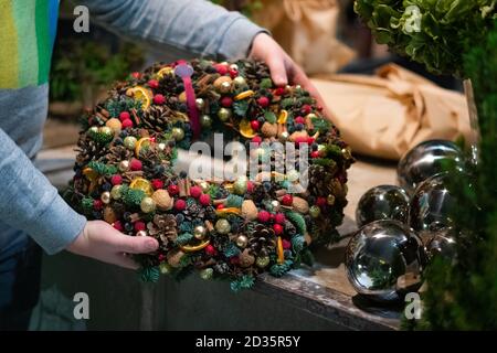 Person hält schöne und bunte Hand gemacht Weihnachtskranz, grüne Fichtenzweige mit Tannenzapfen und andere Dekorationen dekoriert. Weihnachtslch Stockfoto