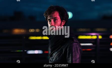 Porträt eines jungen, gutaussehenden Mannes, der draußen vor ihm posiert Der Lichter der Stadt und Blick auf die Kamera Stockfoto