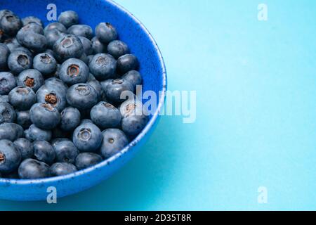 Nahaufnahme der Keramikschale voller Heidelbeeren auf blauem Hintergrund. Reife Blaubeerplatte. Biologische und gesunde Lebensmittel. Stockfoto