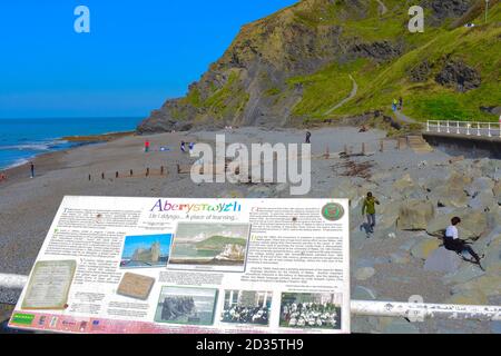 Die Menschen genießen die Sommersonne auf einem Kiesstrand am Constitution Hill, während andere den steilen Weg hinauf zum Gipfel des Hügels gehen. Zweisprachiges Info-Zeichen Stockfoto