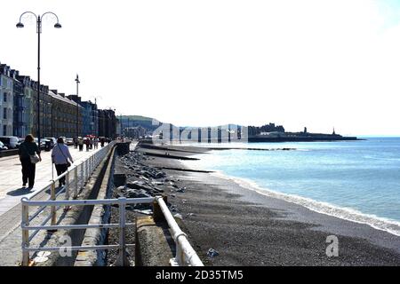 Blick von der Marine Terrace auf den Royal Pier im Badeort Aberystwyth. Menschen, die gerne an der Promenade in der Sonne spazieren Stockfoto