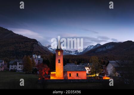 Alte Christentum Kirche in Sils Dorf (in der Nähe von See Sils) in den Schweizer Alpen. Rotes Licht auf Gebäude und die schneebedeckten Berge im Hintergrund. Schweiz, Maloja Region Oberengadin. Landschaftsfotografie Stockfoto