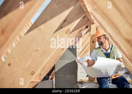 Zufriedener Mann, der eine Blaupause eines neuen Gebäudes hält Stockfoto