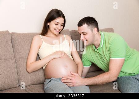 Junger Mann spricht den Bauch seiner schwangeren Frau. Mutterschaftskonzept. Stockfoto