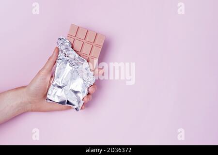 Die Hand der Frau hält eine Tafel rosa Schokolade in Folie. Stockfoto