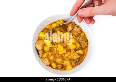 Löffel in der Hand und natürliche Lebensmittel zu Hause gekocht. Ein Teller mit Putenschmorbraten und Kartoffeln auf isoliertem weißem Hintergrund. Ragout von reifen Kartoffeln und Truthahn. Stockfoto
