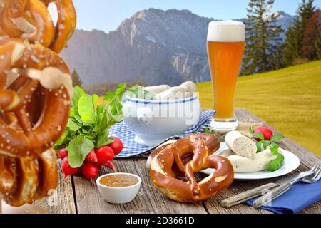 Herzhaftes Frühstück mit Kalbswürsten, frischen Brezeln und einem Weizenbier draußen in den bayerischen Bergen bei Garmisch-Partenkirchen Stockfoto