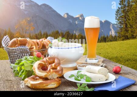 Herzhaftes Frühstück mit Kalbswürsten, frischen Brezeln und einem Weizenbier draußen in den bayerischen Bergen bei Garmisch-Partenkirchen Stockfoto