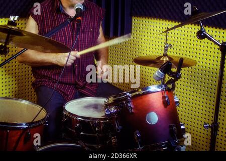 Ein älterer Schlagzeuger spielt in einem Tonstudio. Ein Mann im Alter sitzt hinter einem Schlagzeug mit Stöcken in den Händen Stockfoto