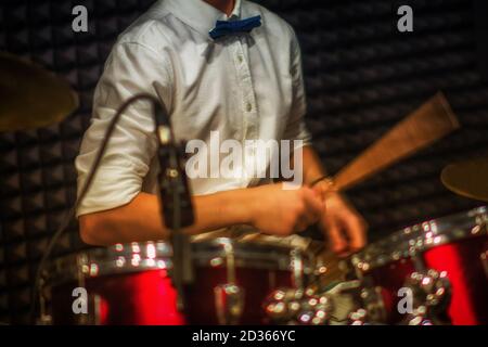 Ein junger Schlagzeuger spielt in einem Tonstudio. Ein Teenager in einem weißen Hemd sitzt hinter einem Schlagzeug mit Stöcken in den Händen Stockfoto