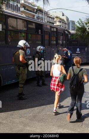 Polizeibeamte sind während eines Protestes in Alarmbereitschaft, während sie das Urteil des Prozesses der Goldenen Morgenröte in Athen, Griechenland, abwarten. Zwei junge Mädchen kommen vorbei. Stockfoto