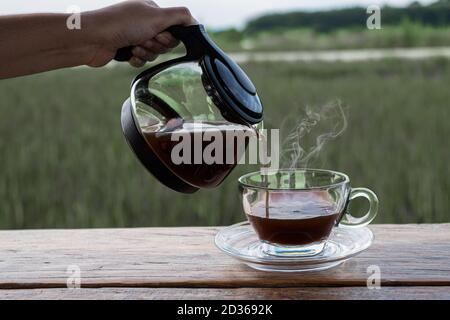 Frau Hand halten eine Kaffeekanne und Tropfen auf das Glas Auf dem Holztisch bei unscharfem Hintergrund Stockfoto