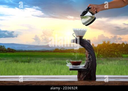 Frau Hand halten eine Kaffeekanne und Tropfen auf die Dropper Glas auf dem Holztropfständer bei Wolke und Blau Himmel Hintergrund Stockfoto