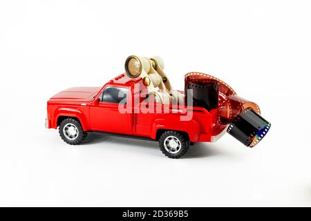 Retro-Opern-Brille und Film im roten trendigen Pickup-Kofferraum. Spielzeugauto, Filmrolle und Retro-Fernglas. Teil des Sets. Stockfoto