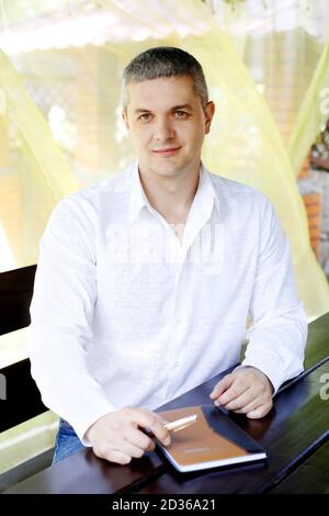 Glücklicher erfolgreicher Mann am Tisch mit Notizbuch (Jotter). Lächelnder Geschäftsmann mittleren Alters Stockfoto
