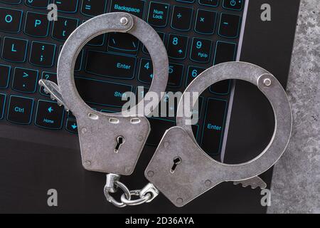 Geschlossene Handschellen auf einer Laptop-Tastatur in Nahaufnahme. Konzept zum Thema Bestrafung für digitalen Betrug Stockfoto