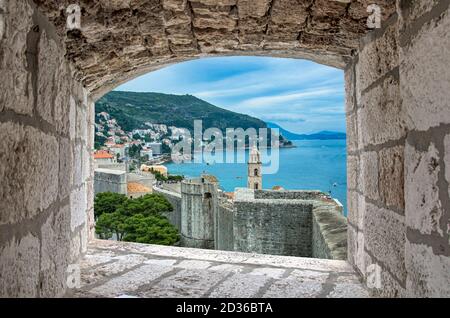 Blick auf Dubrovnik Wand, Turm und blaues Meer während sonnigen Sommertag aus Stein Fenster in Dubrovnik, Kroatien. Atemberaubende Aussicht auf die Stadtmauern von Dubrovnik und Stockfoto