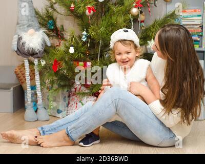 Glückliche Mutter und Baby sitzen in der Nähe weihnachtsbaum Stockfoto