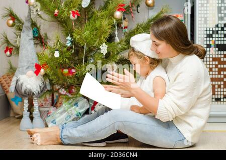 Mutter und Baby lesen Buch in der Nähe von weihnachtsbaum Stockfoto