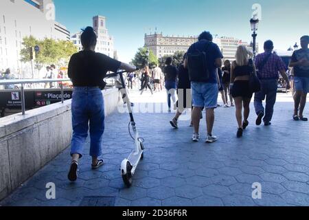 Junge Frau zu Fuß schieben ihren Elektroroller durch die Menge. Barcelona, Katalonien, Spanien. Stockfoto