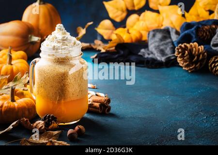 Kürbis gewürzter Latte oder Kaffee im Glas Becher auf blauem Tisch. Heißer Drink im Herbst oder Winter in festlicher natürlicher Tischumgebung Stockfoto