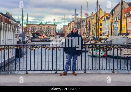 Glücklicher Mann in Winterkleidung steht auf der Nyhavn-Brücke in der Nähe des Nyhavn-Damms in Kopenhagen, Dänemark Stockfoto