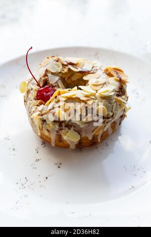 Süßer Donut auf einem Teller auf einem Marmortisch. Ein Teller mit leckeren glasierten Donut mit Schokolade, Nüssen und roter Kirsche. Stockfoto