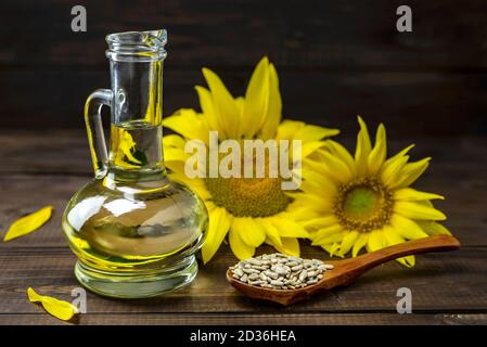 Sonnenblumenöl in der Flasche und geschälte Sonnenblumenkerne auf einem Holzlöffel in der Nähe einer frischen Sonnenblumenkerne auf einem hölzernen Hintergrund. Selektiver Fokus. Stockfoto