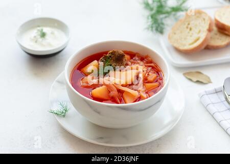 Rote Borschtsuppe in einer weißen Schüssel, serviert mit Sauerrahm, Kräutern und Brot Stockfoto