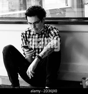 London UK Oktober 06 2020, junger Mann mit EINEM Tattoo Entspannen Rauchen EINER Zigarette mit EINEM Smartphone Stockfoto