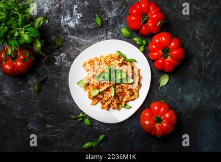 Leckere Pasta mit Hackfleisch und Tomatensauce mit grünem Basilikum auf weißem Teller, dunkler Hintergrund Küchentisch, Draufsicht Stockfoto