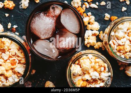 Eis Cola und Karamell Popcorn, ungesunde Speisen und Getränke, schwarzer Tisch, Draufsicht Stockfoto