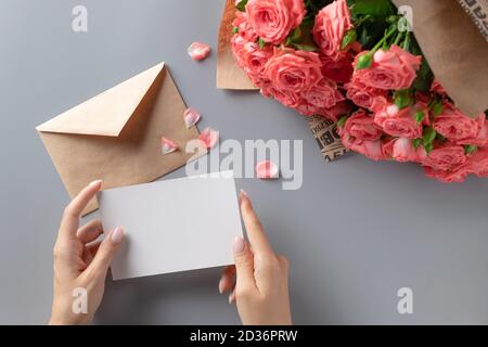 Die Hände der Frau halten eine weiße Karte vor dem Hintergrund Von Blumen Stockfoto