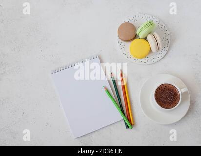 Tasse heiße Schokolade mit Makronen, Notizbuch und Bleistiften Stockfoto