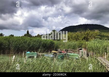 Fischerboote werden am reedy Ufer des Plattensees in Ungarn gegen einen bewölkten Himmel geparkt. Stockfoto