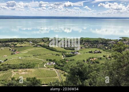 Draufsicht auf den Plattensee mit einem Dorf am Ufer mit einer Wasseroberfläche, die den Himmel mit Wolken reflektiert. Stockfoto