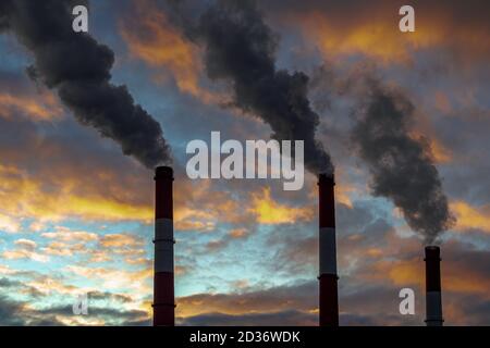 Drei geräucherte Pfeifen auf einem dramatischen, farbenfrohen Himmel. Konzept der Luftverschmutzung Stockfoto