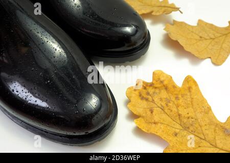 Schwarze Gummistiefel mit Wassertropfen und Eichenlaub auf weißem Hintergrund, selektiver Fokus Stockfoto