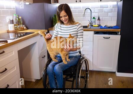 Behinderte junge Frau in der Küche mit Katze auf dem Schoß Stockfoto