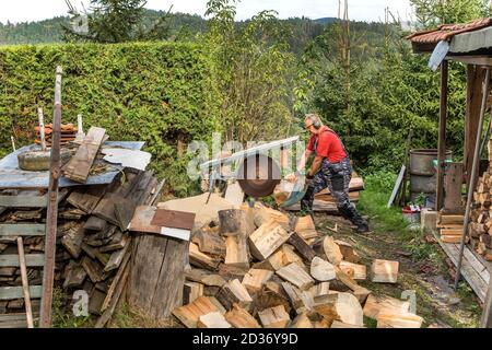 Man schneidet Holz an einer großen Säge. Vorbereitung auf den Winter. Gefährliche Arbeit. Kreissäge. Holzfällerschutzausrüstung. Stockfoto